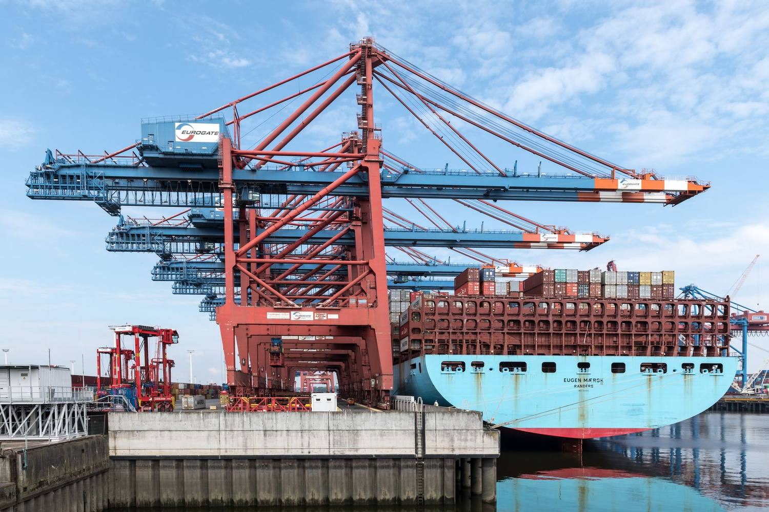 Container terminal with gantry cranes alongside a loaded vessel.